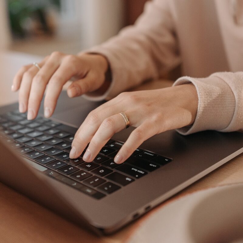A woman sits at a desk typing up cold outreach emails.